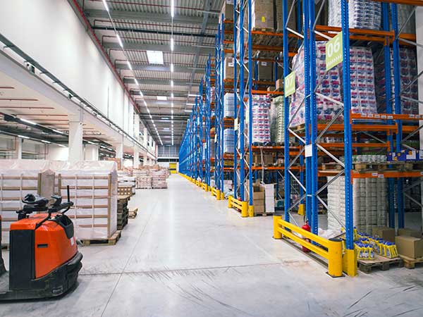 Warehouse storage facility interior. Large distribution center with shelves full of palette boxes and forklift machine. Posa-di-film-estensibile